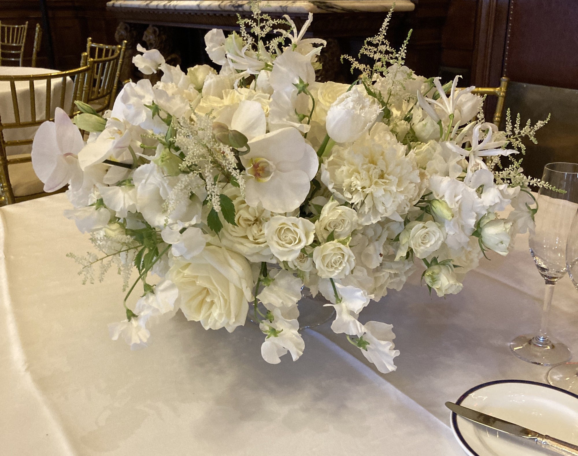 Low centerpiece of white roses, orchids, and sweet pea