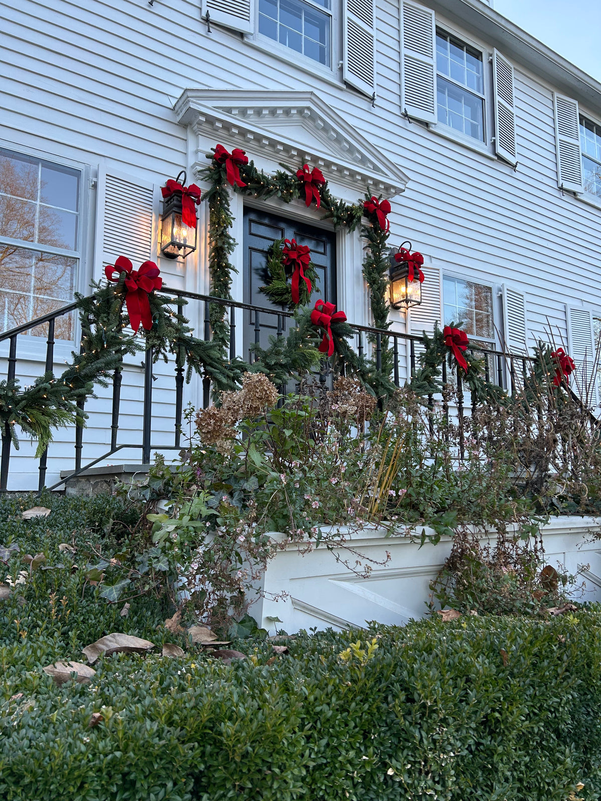 Front entry dressed with fresh garland, a wreath and red velvet bows