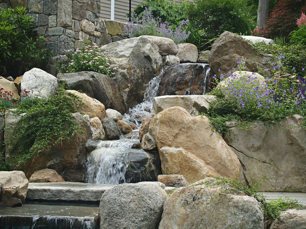 Natural stone waterfall with flowering borders — representative of custom water feature work