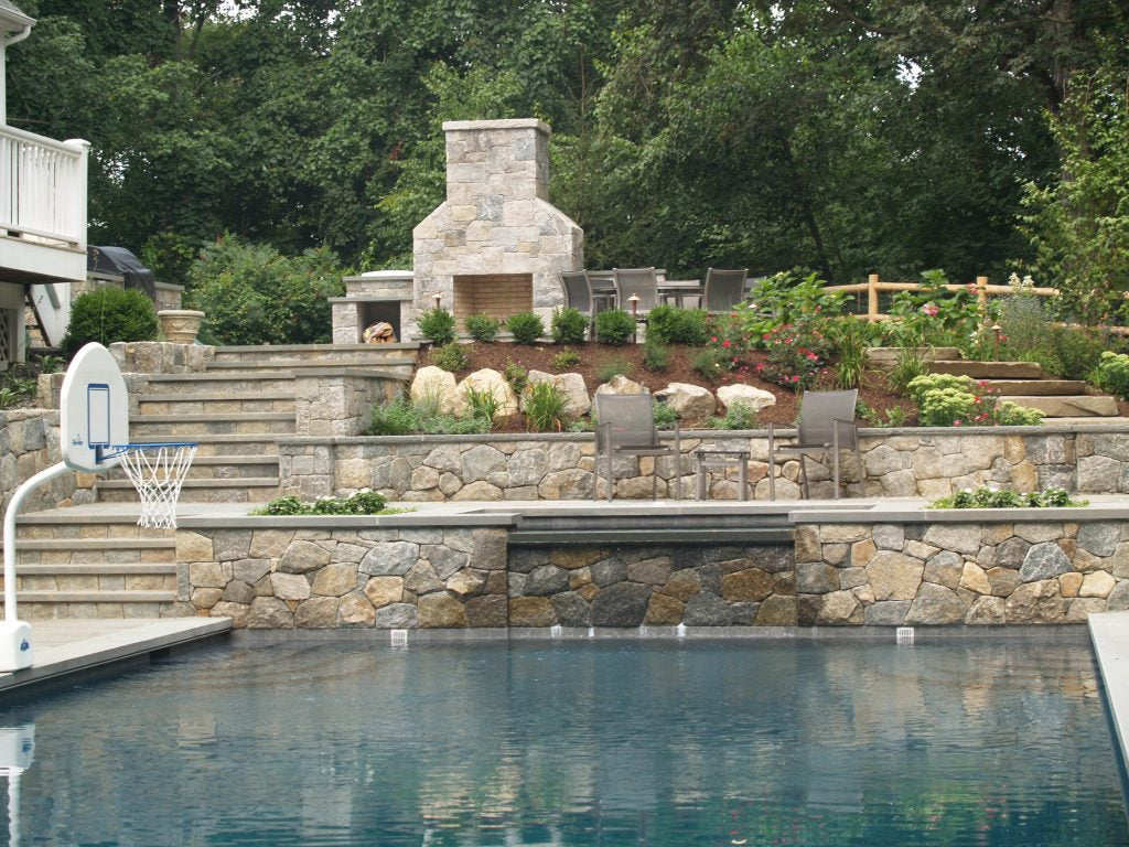 Outdoor setting with a pool, stone wall, and garden area.